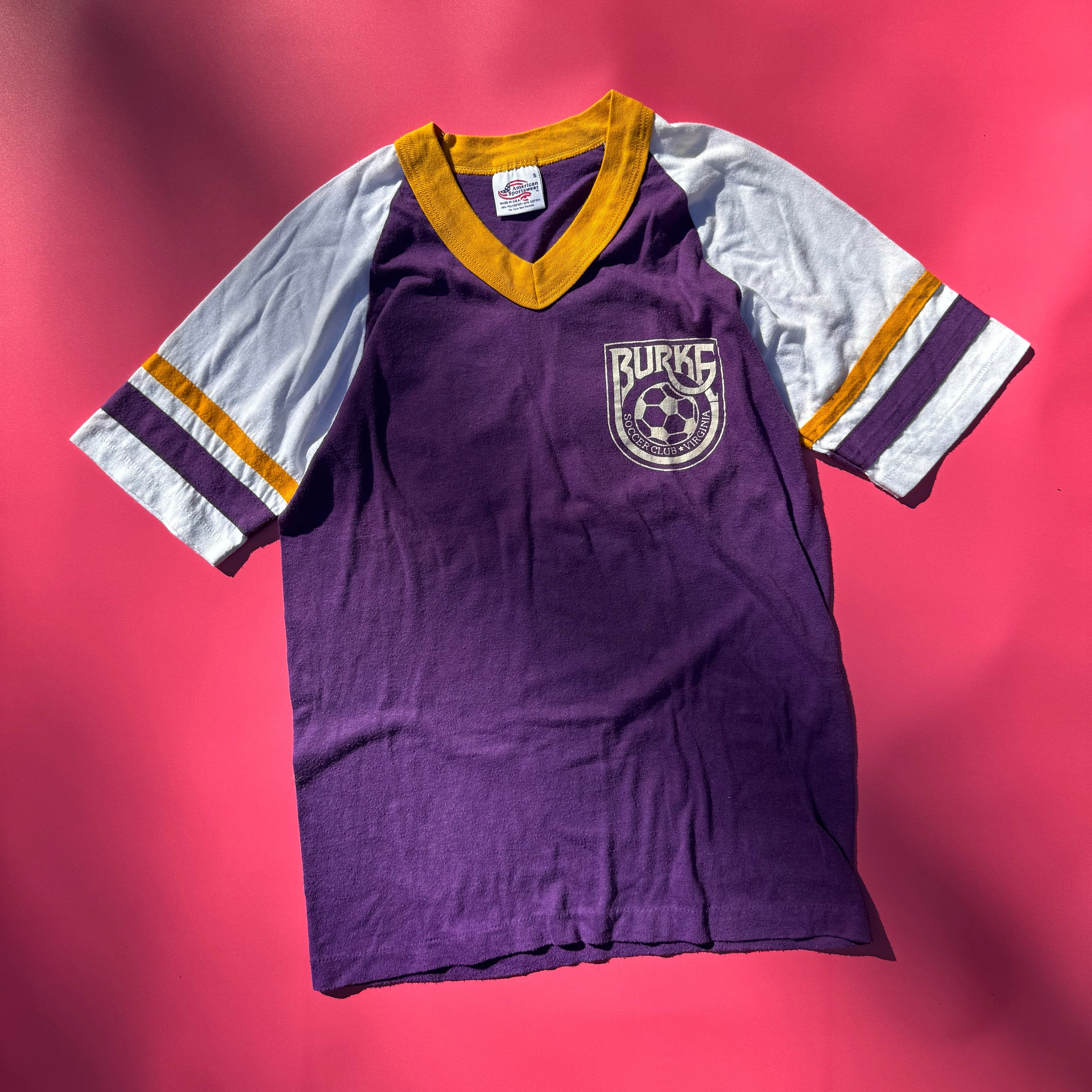 Purple and white sports shirt with a logo on a pink background
